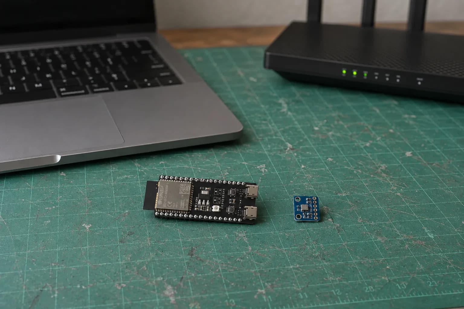 An ESP32-S3-DevKitC-1, BME280 module, and Wi-Fi router beside a MacBook Pro before network setup.