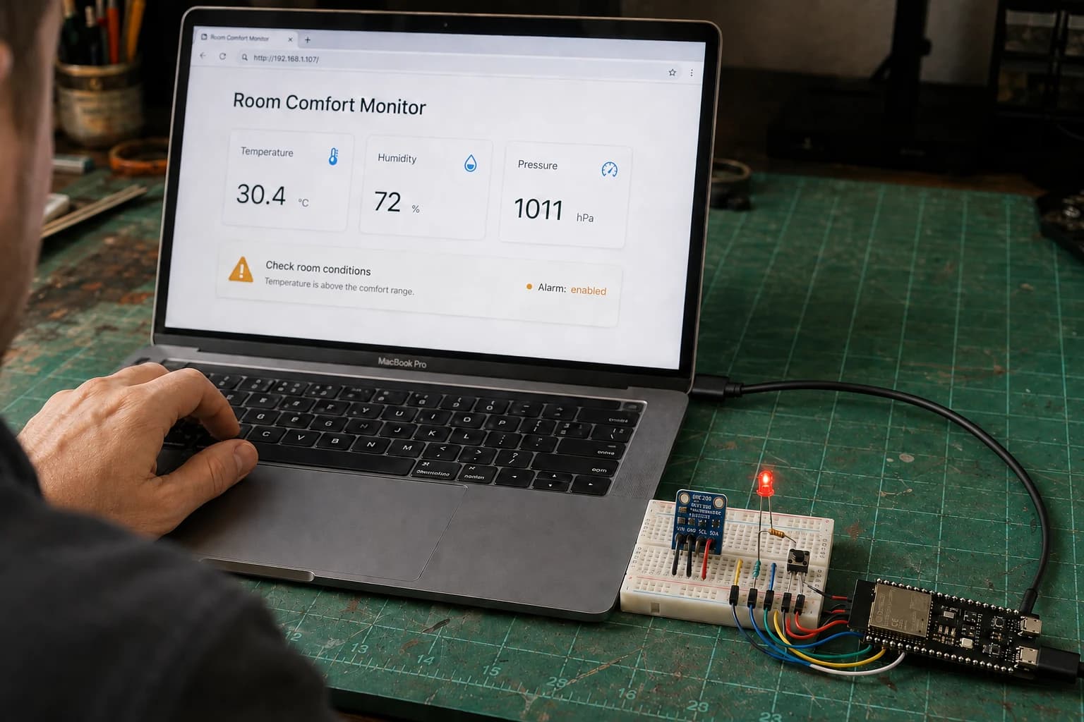 MacBook Pro hiển thị dashboard Room Comfort Monitor cạnh prototype ESP32-S3 được cấp nguồn đúng bằng cáp USB-C.