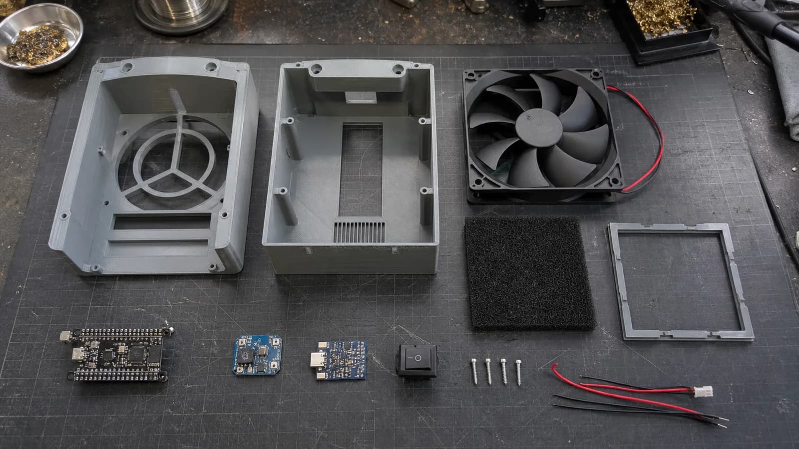 A 120 mm PC fan, carbon filter, ESP32-C3, control board, and 3D-printed enclosure parts laid out on a workbench.