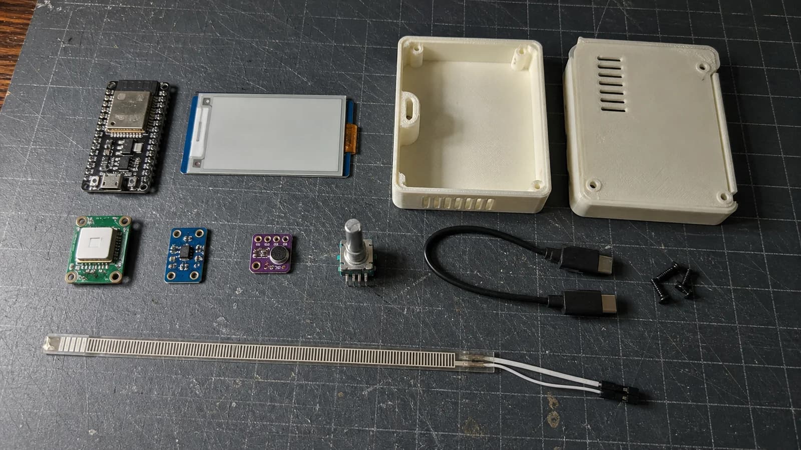 An ESP32-S3, e-paper display, SCD41, light sensor, MEMS microphone, encoder, and 3D-printed clock enclosure on a workbench.