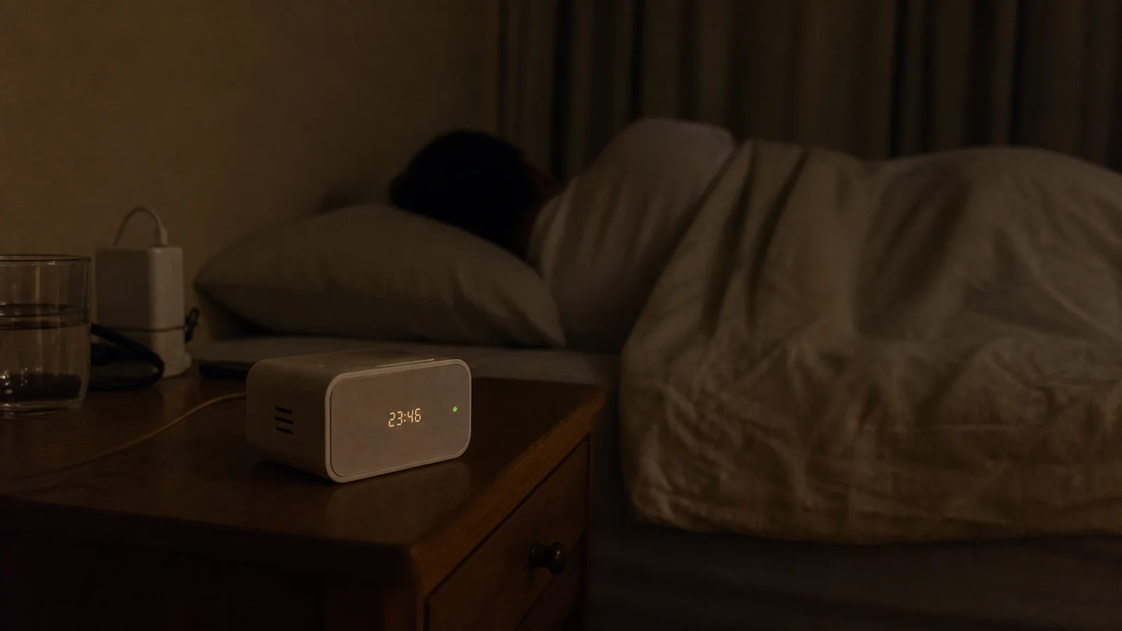 A camera-free sleep indicator clock on a nightstand with an extremely dim display while someone sleeps.