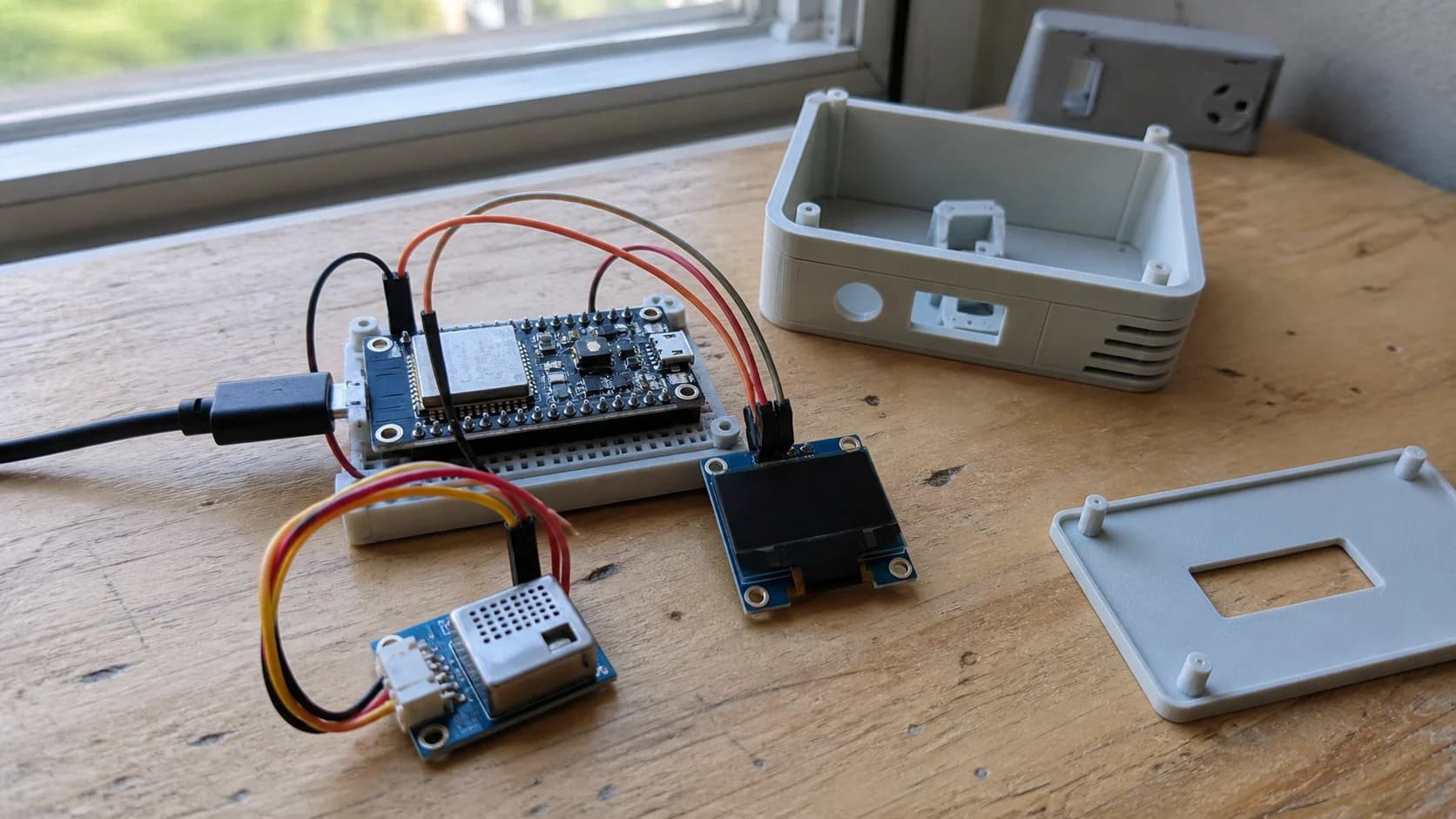 Prototype window reminder device with an ESP32 board, SCD40 or SCD41 CO2 sensor, OLED display, and a 3D-printed enclosure on a desk near a window.